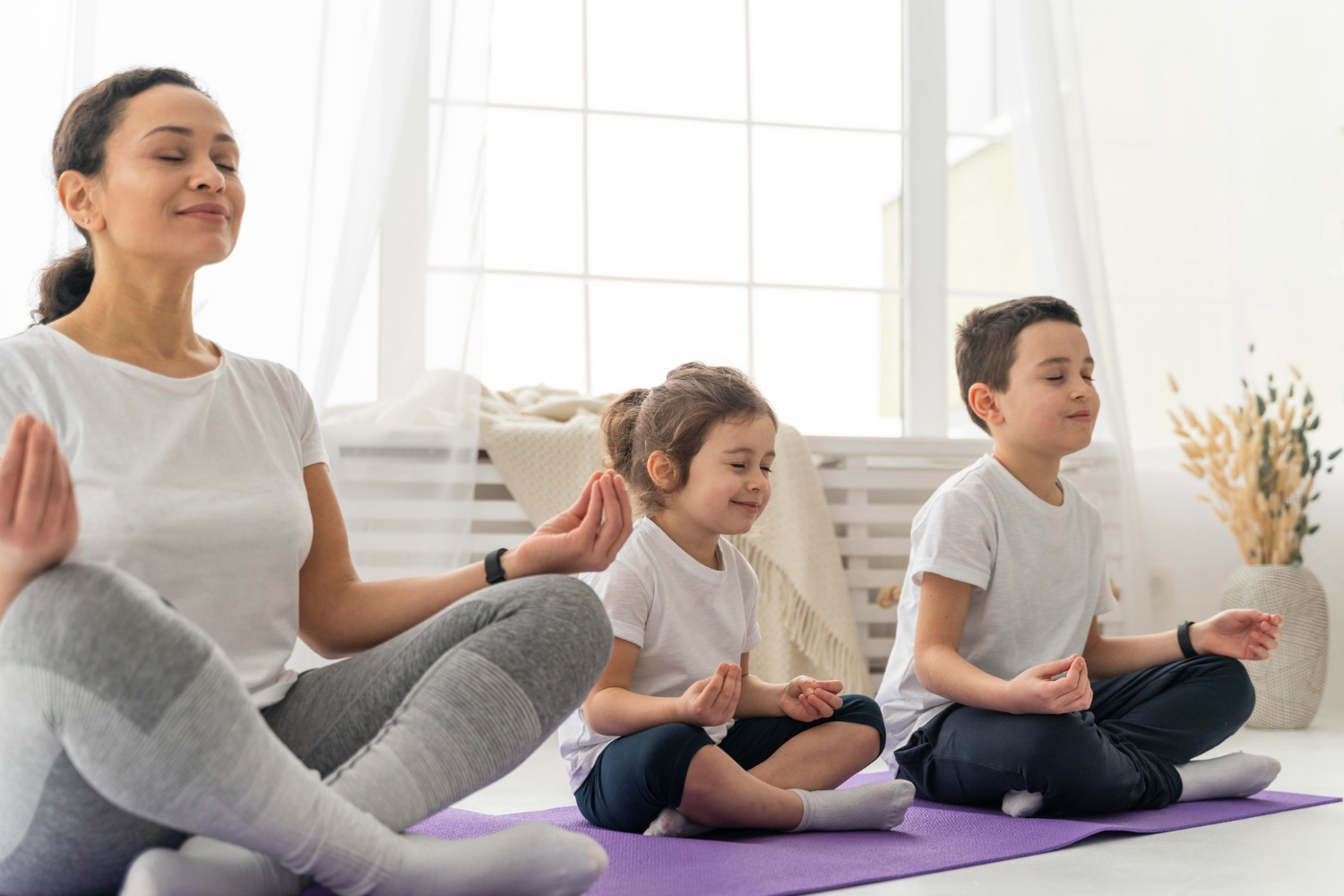 2 enfants assis sur un tapis en train de suivre un cours de yoga avec une femme adulte